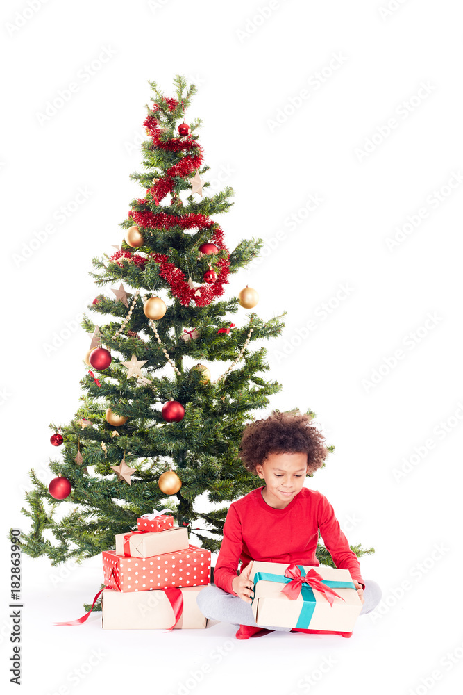 Portrait of cute mixed race little boy sitting on floor near Christmas tree with gift box in his hands