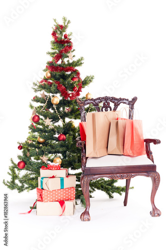Empty chair with shopping bags on it near Christmas tree and stack of gift boxes on white background