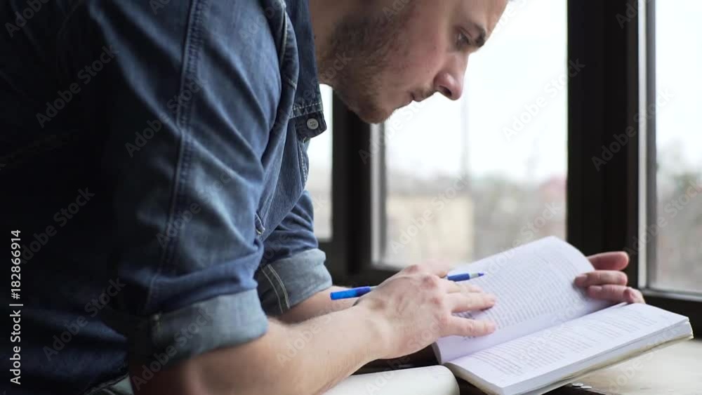 Pan of young man studying near the window Pan of young man studying near the window