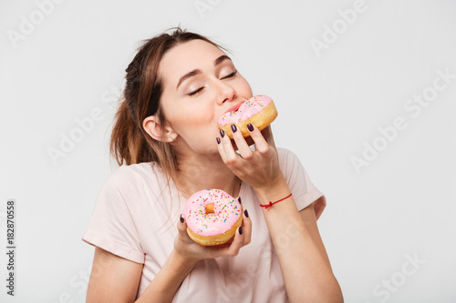 Fotobehang Close up portrait of a satisfied pretty girl eating donuts
