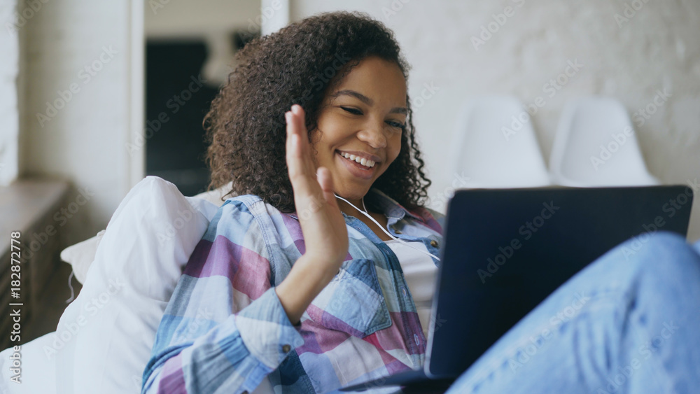 Cheerful mixed race girl having video chat with friends using laptop camera  while lying on bed Stock Photo | Adobe Stock