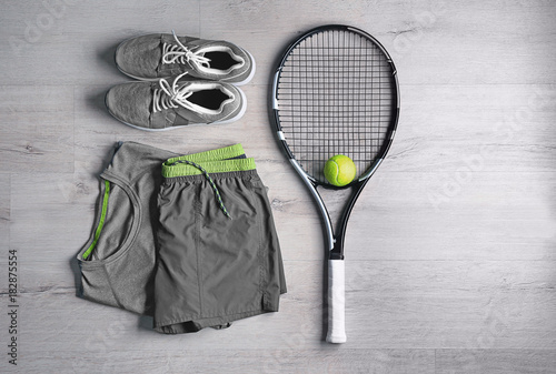 Tennis racket, ball, clothes and shoes on wooden background