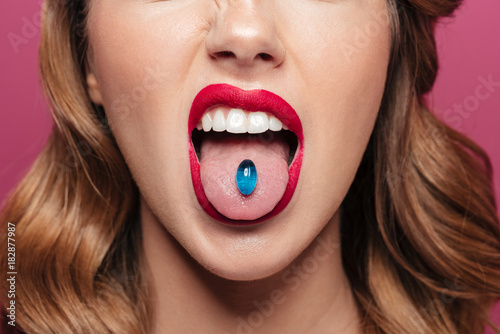 Canvastavla Cropped image of young lady with blue lips holding pill in mouth