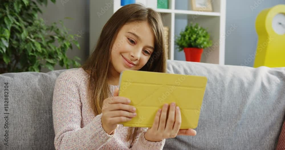 Pretty teenager girl using her tablet computer, scrolling and taping on it while sitting on the grey couch in the nice room. Insude Pretty teenager girl using her tablet computer, scrolling and taping on it while sitting on the grey couch in the nice room. Insude