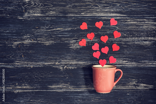 Pink cup on a wooden old background with red hearts. Valentine's Day. Photo with toning. photo