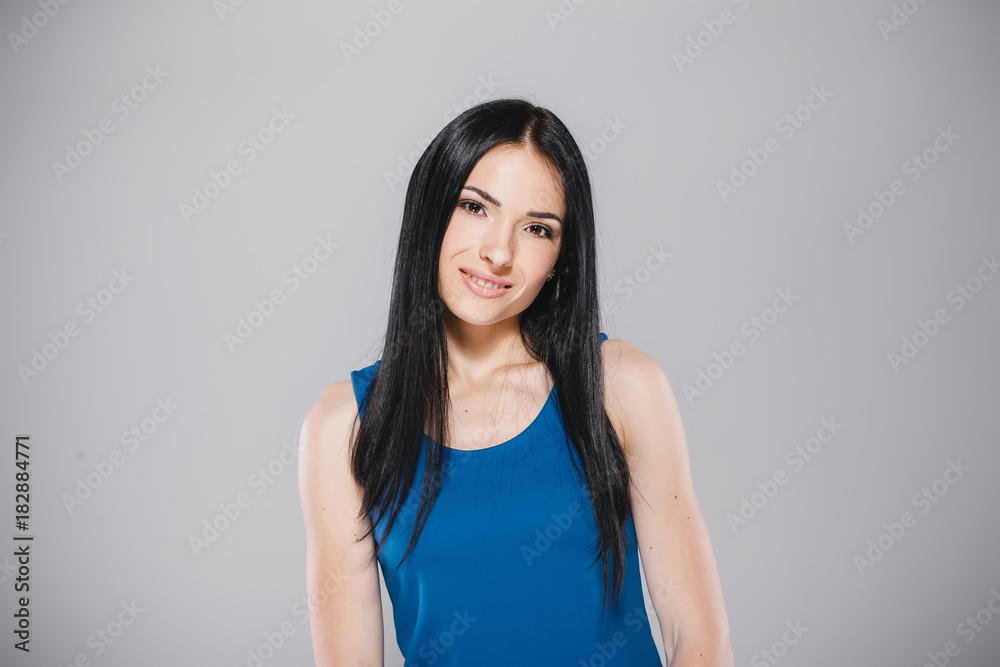 young woman with long brunette hair in blue dress smiling in photostudio on gray background young woman with long brunette hair in blue dress smiling in photostudio on gray background