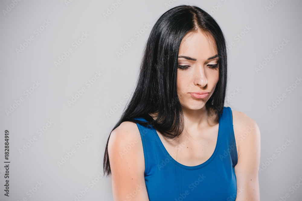 young upset model with long brunette hair in blue dress in photostudio on gray background young upset model with long brunette hair in blue dress in photostudio on gray background