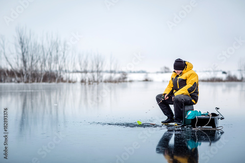 Man ice fishing on a frozen lake.