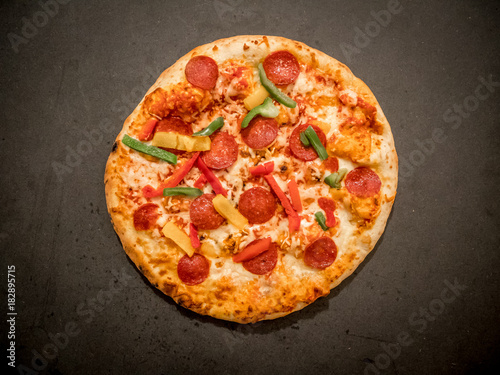 Top view of salami pizza on dark background.