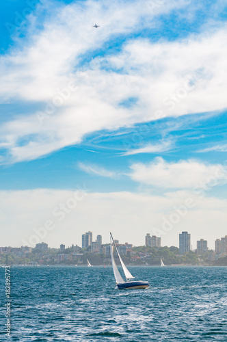 Yacht with Sydney cityscape on the background and plane in the sky