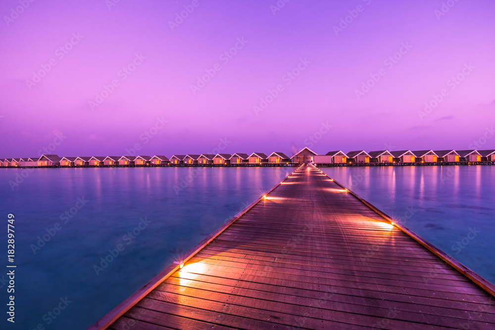 Sunset on Maldives island, water villas resort. Beautiful sky and clouds. Beautiful beach background for summer travel with sun, beach wooden jetty. Summer mood sun beach background concept.