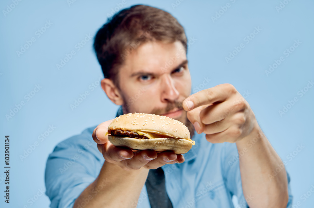 Man with a beard on a blue background holds a hamburger, fast food, portrait