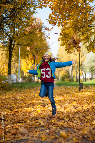 Little girl throws up the autumn leaves and jumps