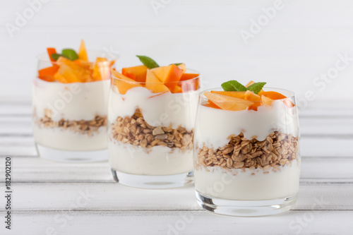 Persimmon creamy trifle in beautiful glasses, fresh ripe fruit slices on white wooden background. Healthy vegetarian food. Delicious dessert. Close up photography. Selective focus.