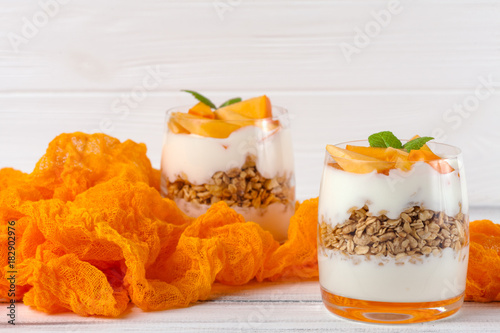 Persimmon creamy trifle in beautiful glasses, fresh ripe fruit slices on white wooden background. Healthy vegetarian food. Delicious dessert. Close up photography. Selective focus.