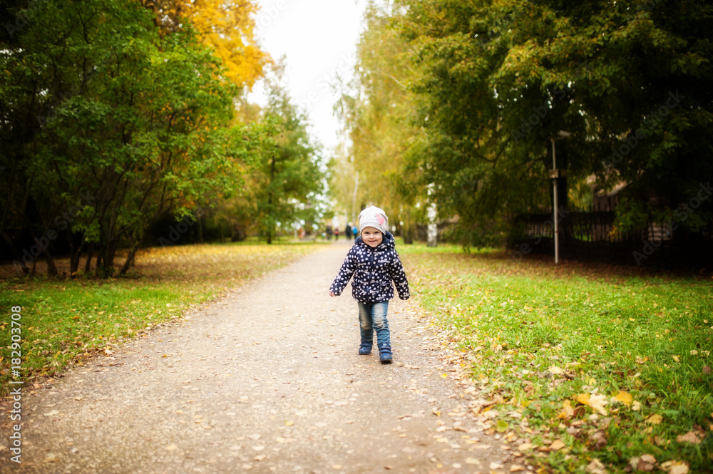 the baby runs along the asphalt road in autumn in the park