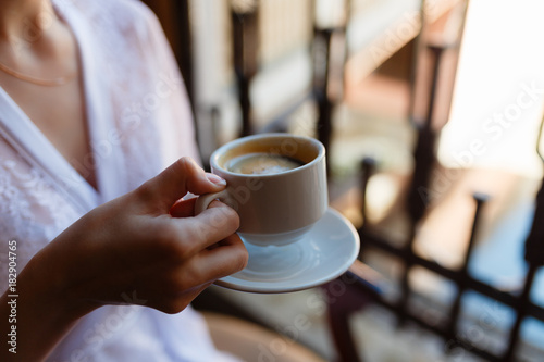 Young girl in Bathrobe with a pattern, drinking coffee on the hotel balcony, enjoying the view and the awakening. Morning girl drinking espresso. Close-up view.