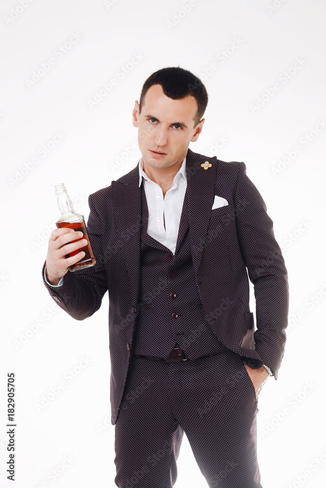 Confident young man with stylish haircut holding a bottle of whiskey and looking away Confident young man with stylish haircut holding a bottle of whiskey and looking away