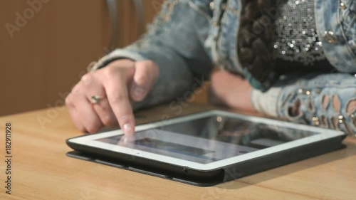 Close-up of unknown woman dressed in denim jacket sits at desk at office the resting and looking at favorite photos using the screen of computer tablet in white-black colour. photo