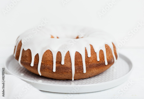 Homemade lemon bundt cake with thick lemon icing on light grey plate with coth napkin and cake forks on white wooden table photo