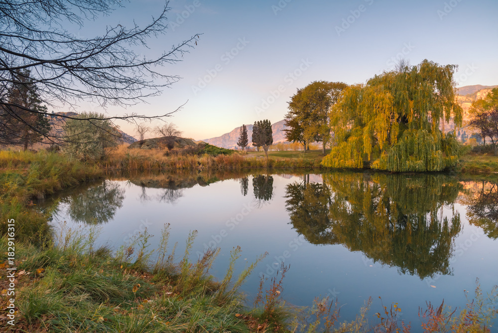 Peaceful pond at sunset with reflections of surrounding trees in autumn
