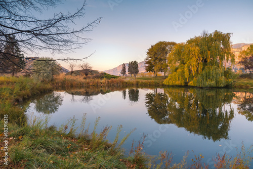 Peaceful pond at sunset with reflections of surrounding trees in autumn