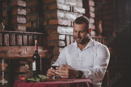 A handsome young man sits in a restaurant waiting for his girlfriend with wine and rose.
