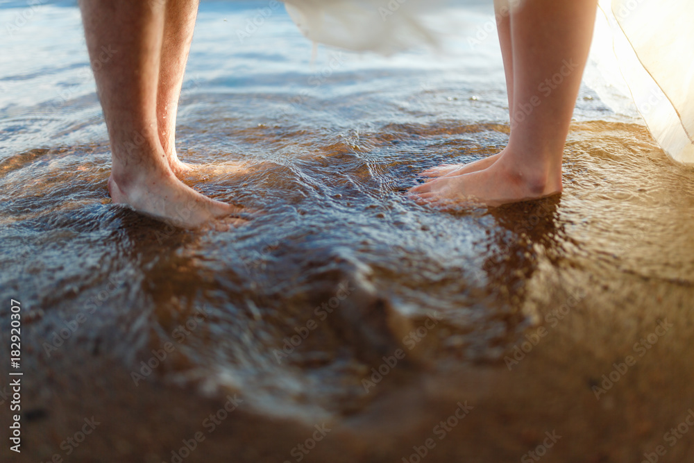Closeup legs of loving couple on the beach, near the water, standing on the sand. Stand in front of each other in the wet sand, enjoying the waves from the wind. Closeup legs of loving couple on the beach, near the water, standing on the sand. Stand in front of each other in the wet sand, enjoying the waves from the wind.