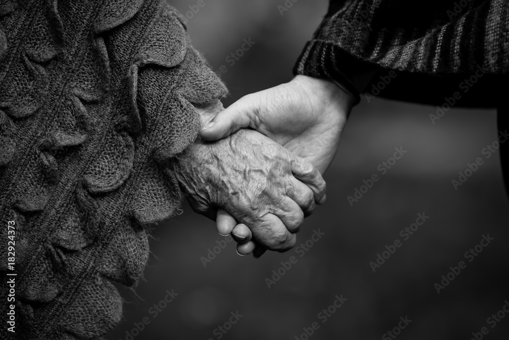 Holding two people hands young and old closeup black and white picture.