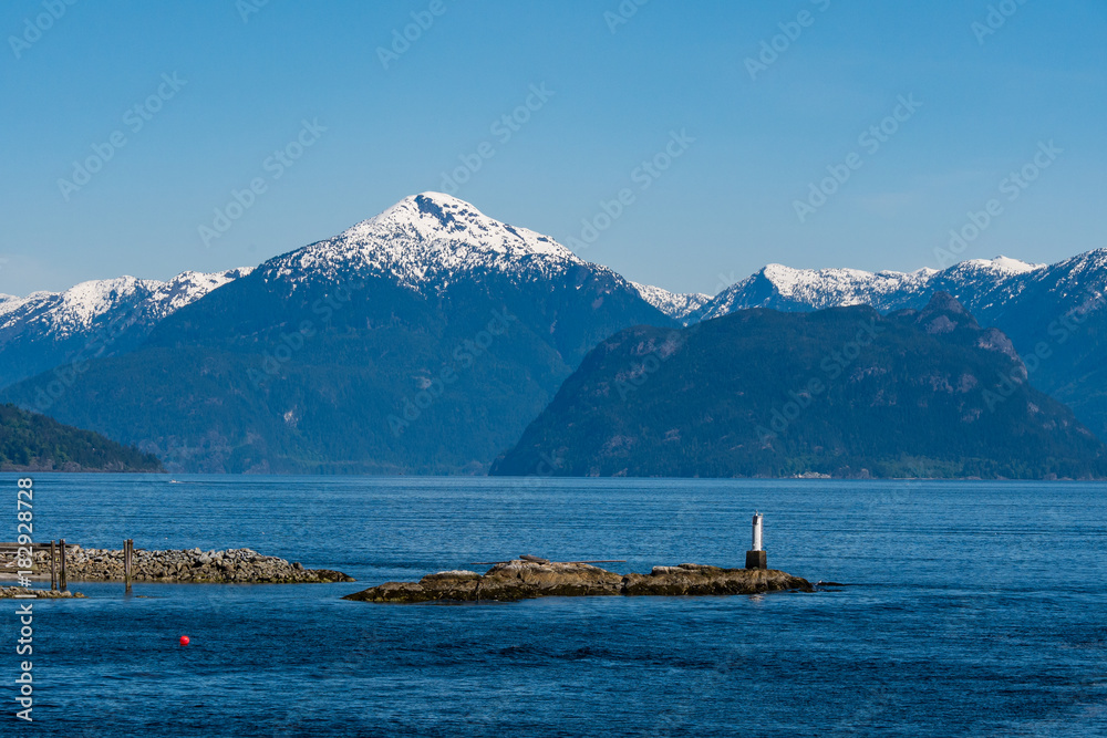 snow covered mountains surrounded ocean with light house in forground