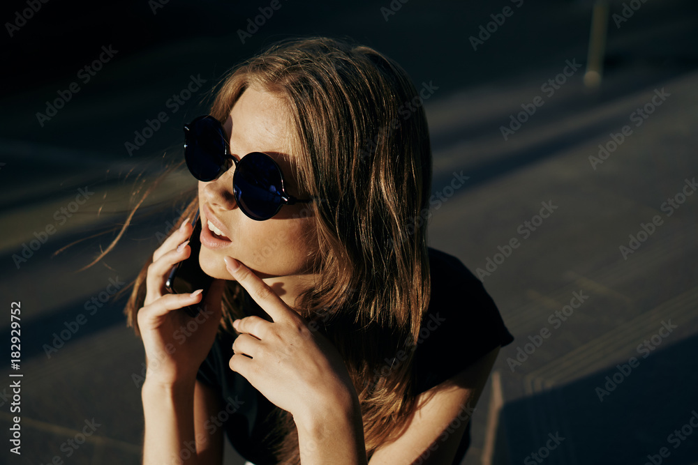 Young beautiful woman in round sunglasses on the street in the city is calling by phone Young beautiful woman in round sunglasses on the street in the city is calling by phone