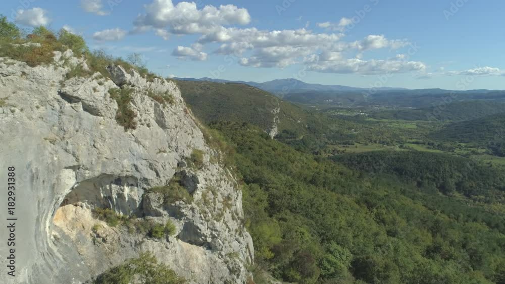 AERIAL: Flying above karst landscape on sunny summer day. Green forest and rocky hills under blue skies. Flying past the rocky cliff towards meadow valleys and hills overgrown by lush woods in spring AERIAL: Flying above karst landscape on sunny summer day. Green forest and rocky hills under blue skies. Flying past the rocky cliff towards meadow valleys and hills overgrown by lush woods in spring