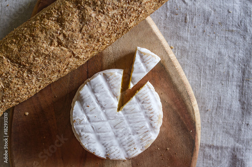 Foto The Swiss Camembert formed cheese and a triangular piece of cheese on a wooden textured board and a grain baguette on a woven canvas background