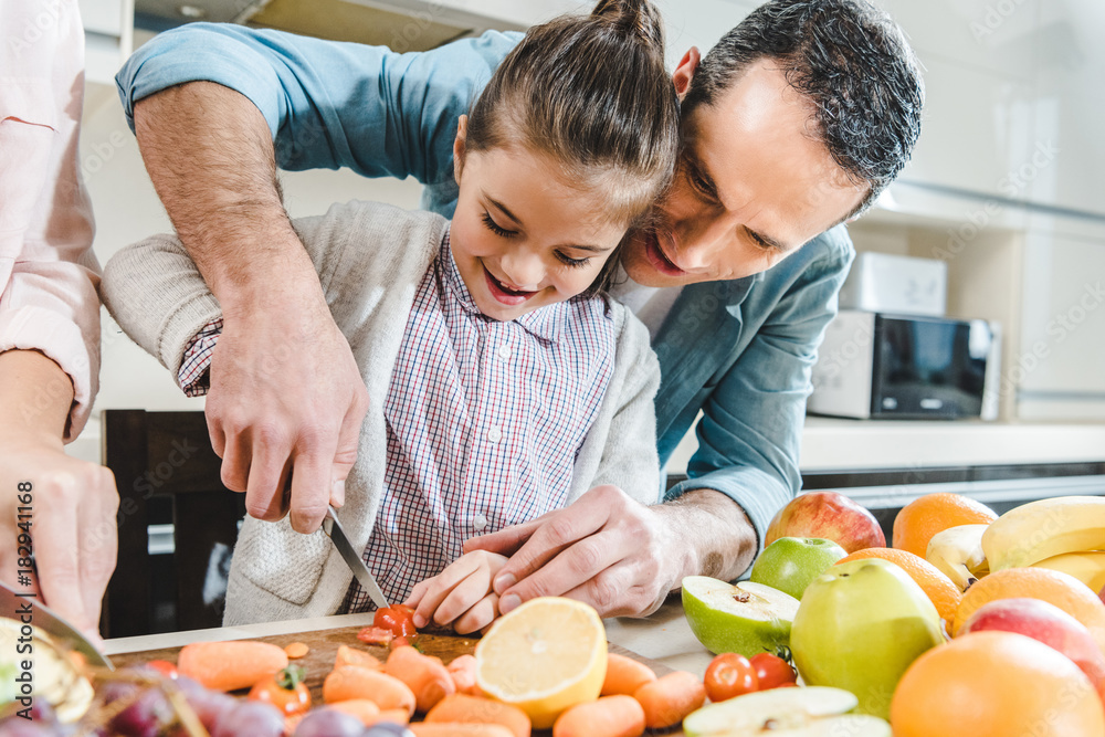 father with daughter slicing vegetables and fruits