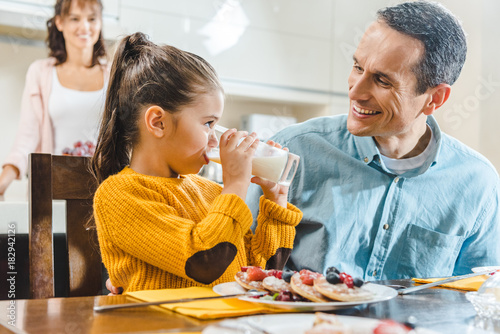 Fotografía happy family at kitchen, daughter with father sitting at table with pancakes and