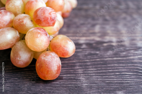 Close-up part of wet tassel of ripe yellow-green-red grapes is lying on old dark wooden table with copy space.