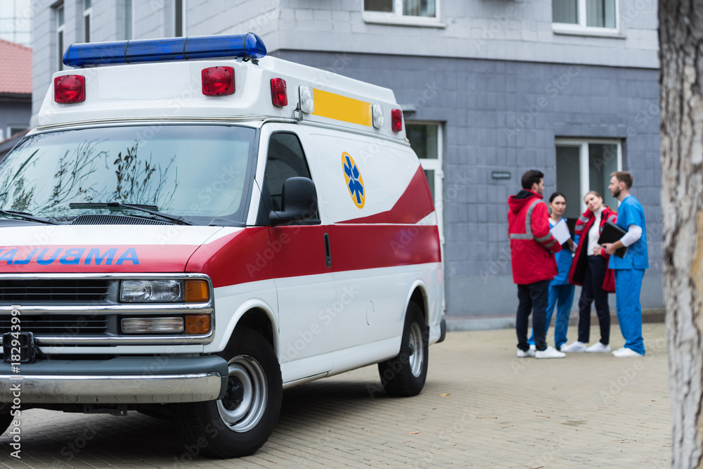 Four ambulance doctors talking and standing near car Four ambulance doctors talking and standing near car