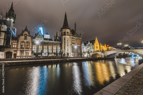 Ghent, Belgium - January, 3th, 2017. Saint Michael's bridge view with houses and Clock tower on Graslei embankment reflected in canal by evening lights. Gent night illumination. Long exposure shot.