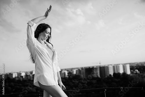 Portrait of an outstanding woman in white male shirt posing on top of the building with charming scenery on the background. Black and white photo. © AS Photo Family