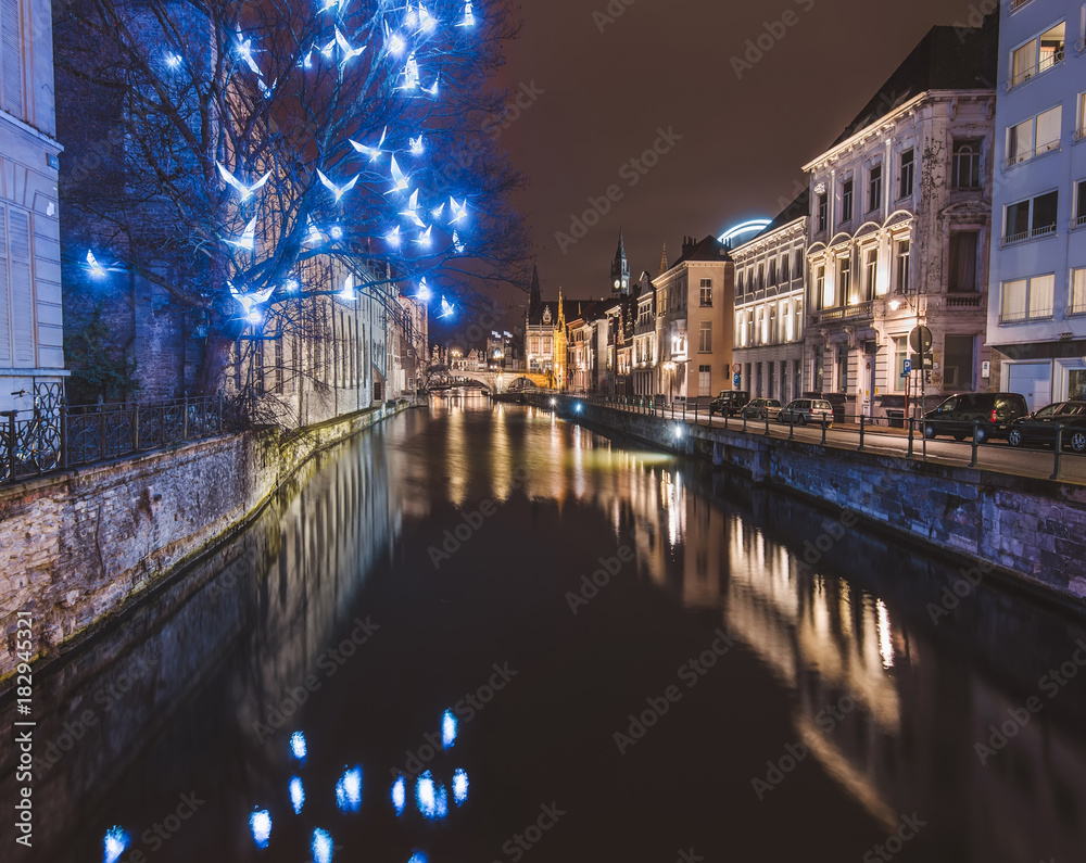 Ghent, Flanders, Belgium - January 3th, 2017. Christmas illuminated birds installation and medieval houses reflected in night canal by evening illumination in historical Gent city center by night.