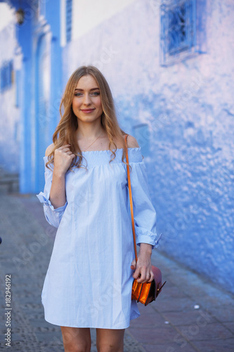 Beautiful woman in blue summer dress stands on a blue street of Morocco © IVASHstudio