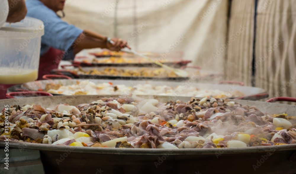 People are preparing a giant paella. Adding seafood to huge frying pans. People are preparing a giant paella. Adding seafood to huge frying pans.