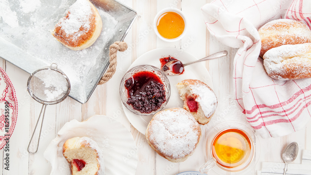 Tea time with festive sufganiyot donuts filled with jelly and covered with sugar powder. White wooden background, bright lighting. Banner composition. Tea time with festive sufganiyot donuts filled with jelly and covered with sugar powder. White wooden background, bright lighting. Banner composition.