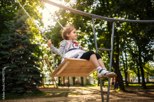 Cute little girl on a swing. Smiling child playing outdoors in summer.