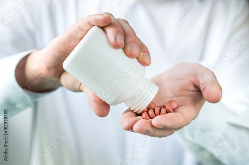Doctor, pharmacist or pharmaceutical representative with white tablets. Man in white coat pouring spilling pills to hand palm from medicine bottle.