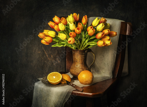 Classic still life with bouquet of tulips flowers placed on rustic wooden chair with fresh oranges and scarf 