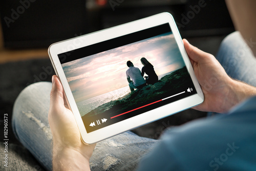 Online movie stream with mobile device. Man watching film on tablet with imaginary video player service. photo