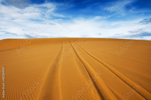 Bright yellow sand empties against the blue sky with clouds. The arid region of the planet