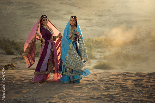 Two happy women wearing Iran or Arabian traditional dress stand by the sand.