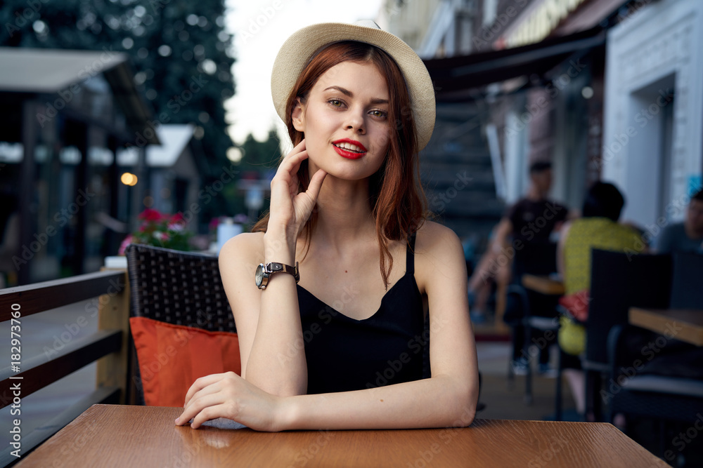 Young beautiful woman in a hat sits at a table in a cafe on a street in the city